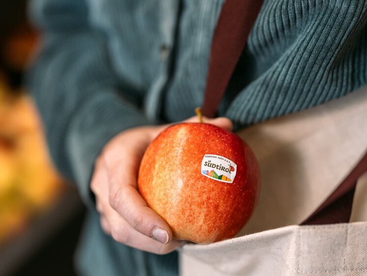 © IDM Südtirol/Hannes Unterhauser A red apple with a sticker label Südtiroler Apfel PGI being placed inside a fabric bag. | © IDM Südtirol/Hannes Unterhauser