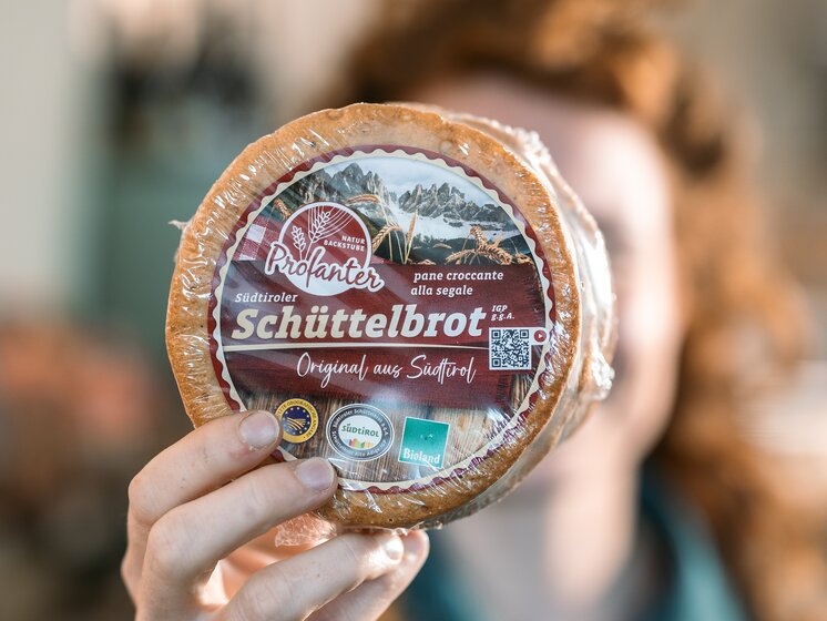 © IDM Südtirol/Hannes Unterhauser Schüttelbrot Profanter with the PGI South Tyrolean Schüttelbrot logo on the package, held in front of a person's face | © IDM Südtirol/Hannes Unterhauser