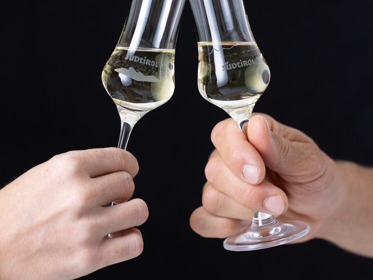 © IDM Südtirol/Hannes Unterhauser Two engraved grappa glasses in a toast: one featuring the South Tyrol brand wordmark and panorama, the other featuring the South Tyrol brand wordmark and stylized panorama | © IDM Südtirol/Hannes Unterhauser